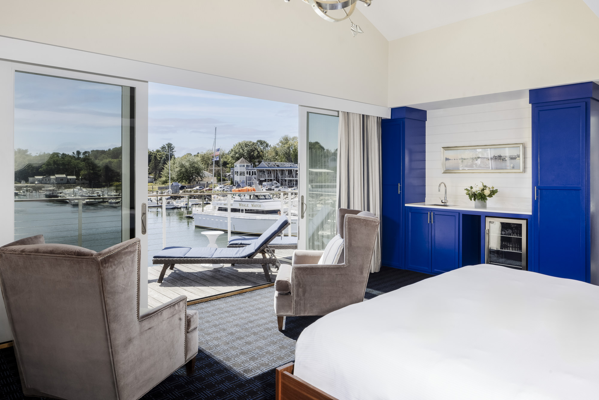 Hotel room with large windows overlooking a marina, two chairs, and a blue cabinet.