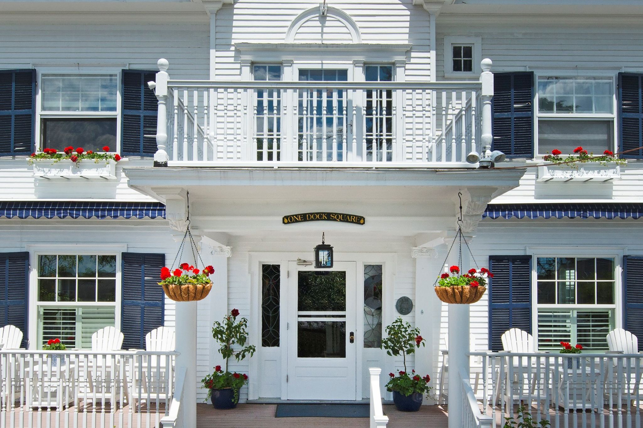 White house entrance with blue shutters, flower baskets, and plants.