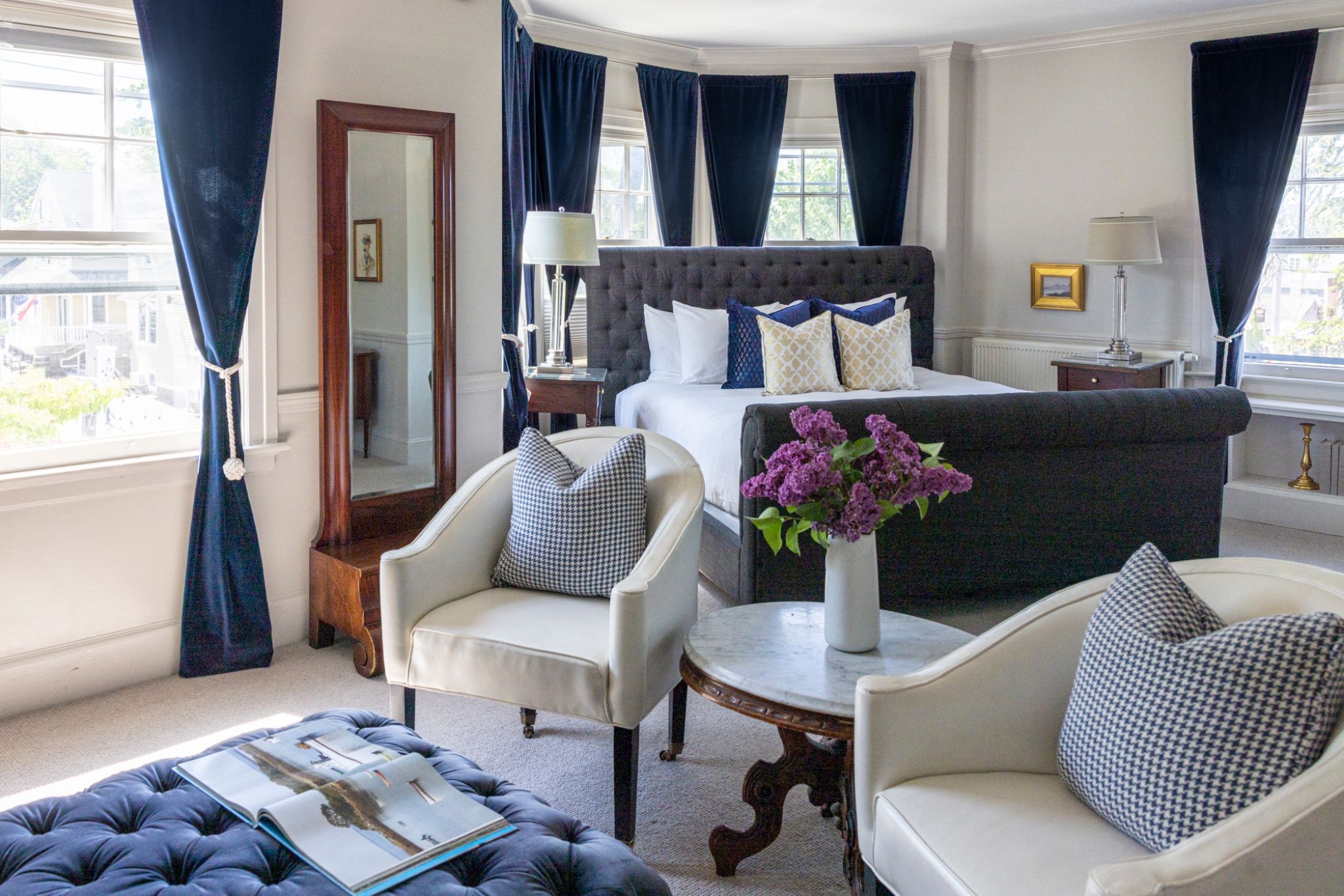 Elegant bedroom with blue curtains, white chairs, and a tufted bed.
