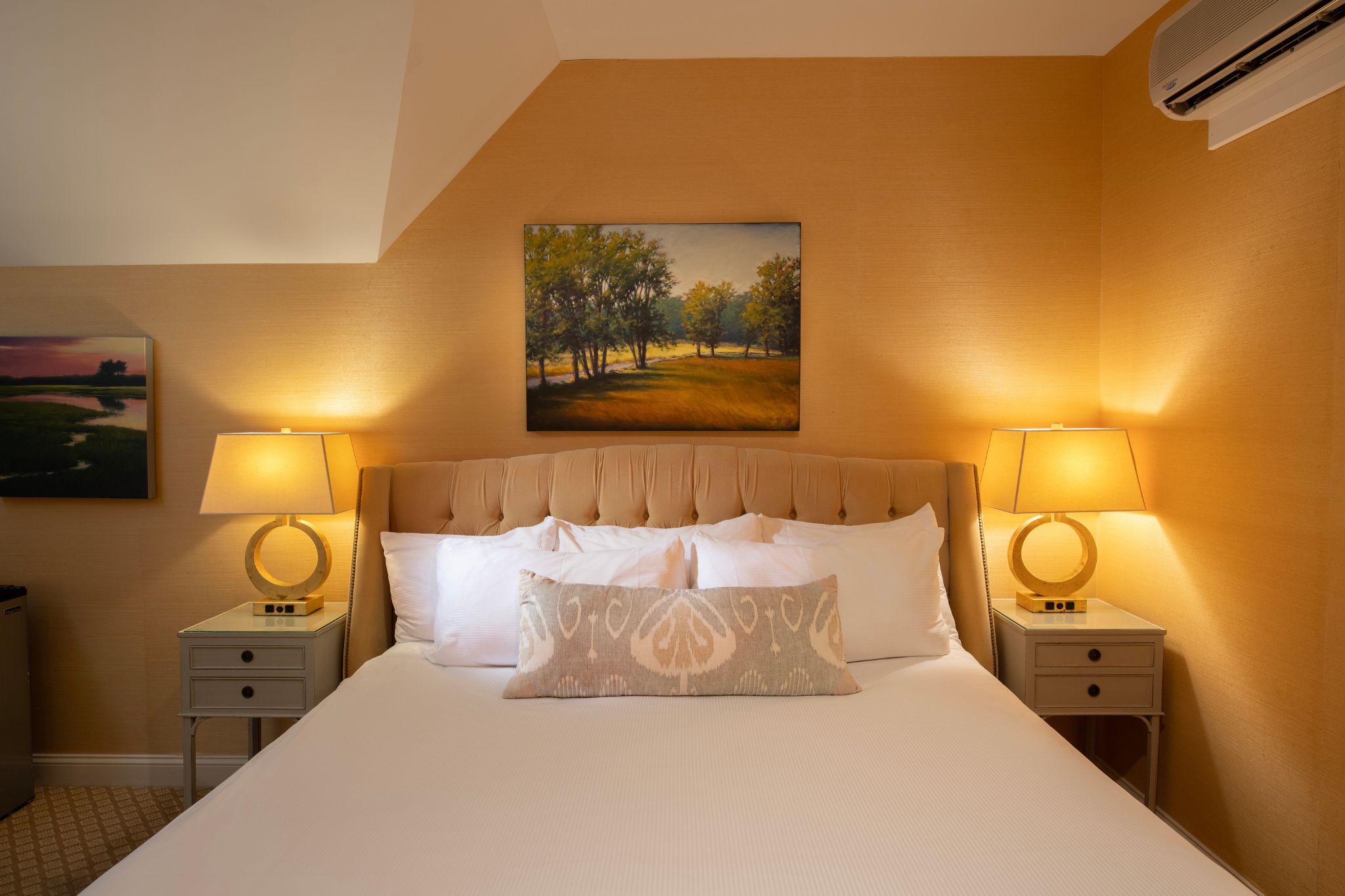 Cozy bedroom with a large bed, soft lighting, and framed landscape artwork.