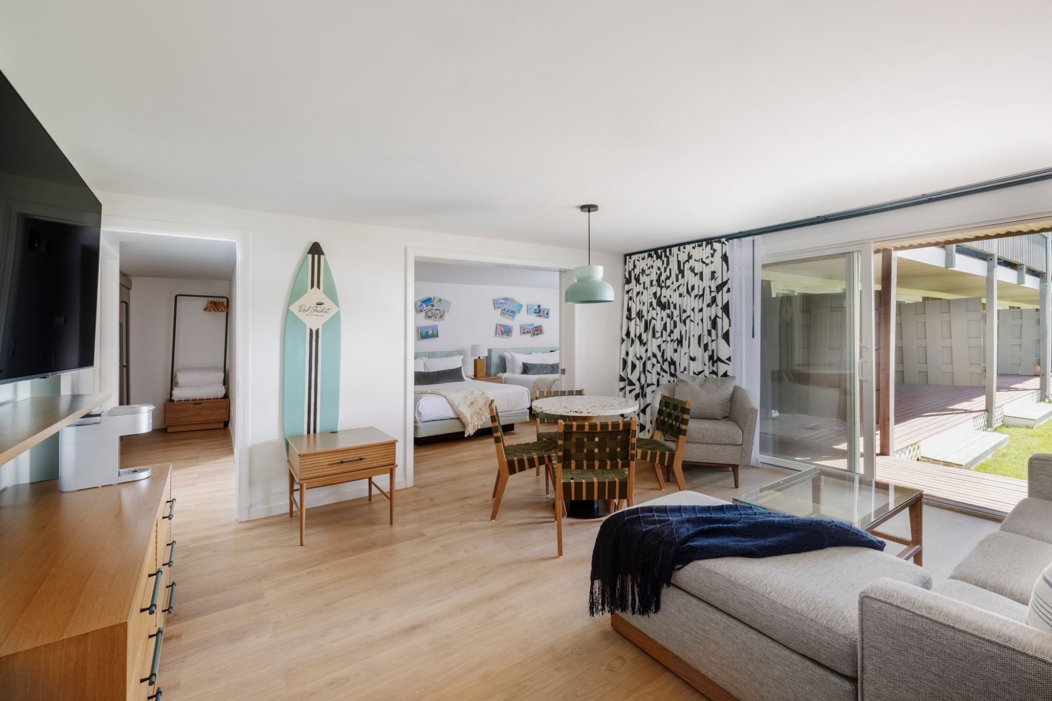 Spacious modern living room with wood floors, large sofa, and open glass doors to a patio.