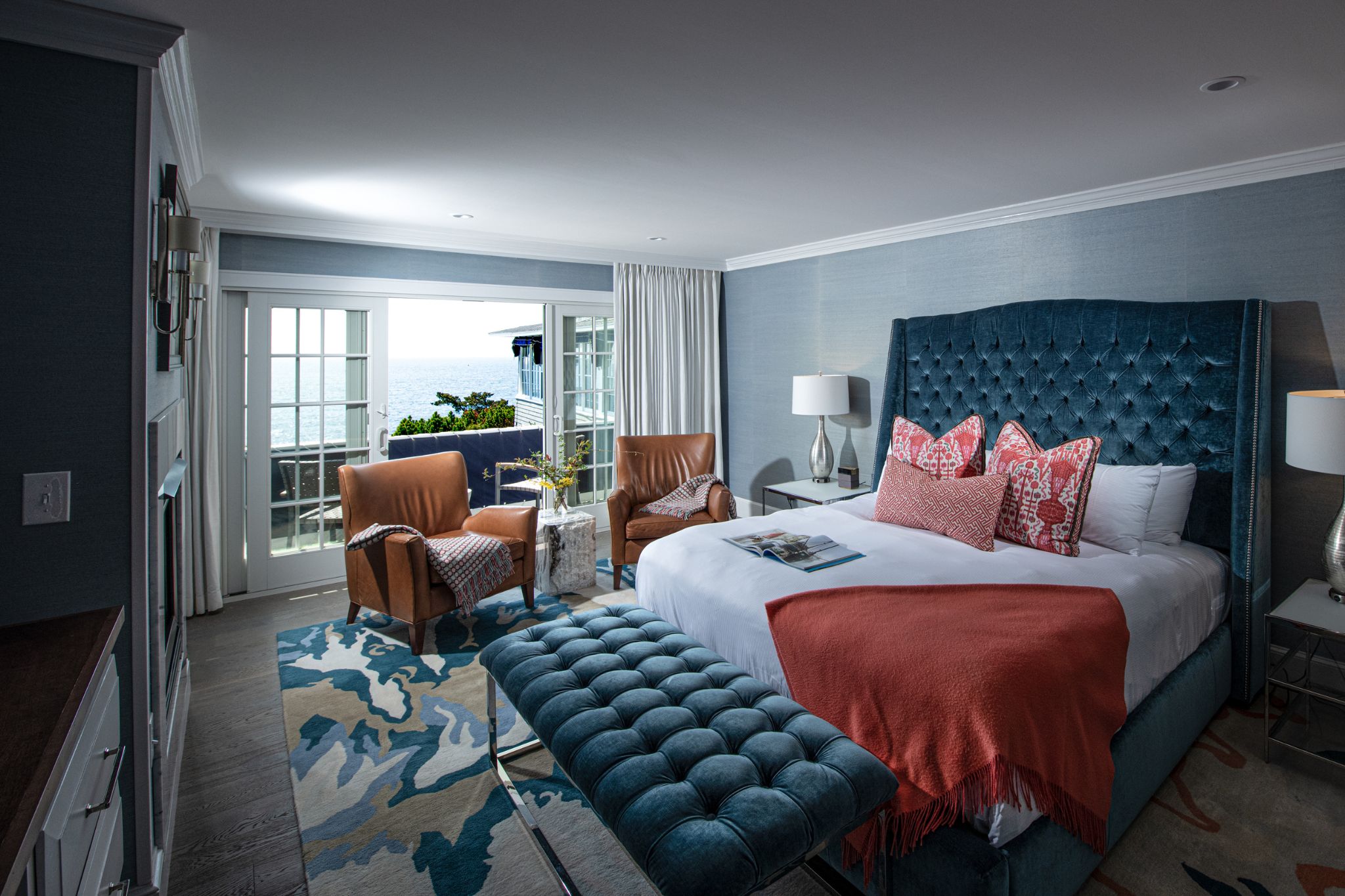 Elegant hotel room with a sea view, blue and coral accents, and plush seating.