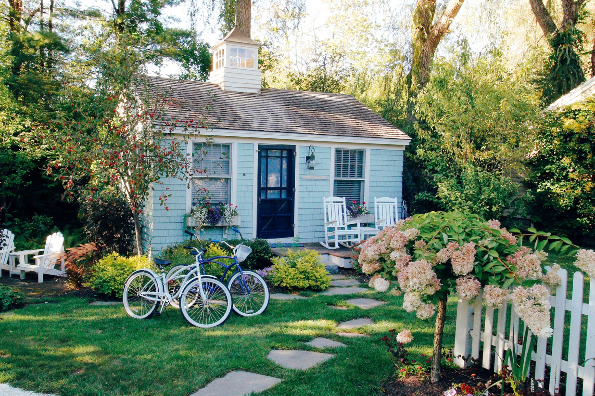 Cozy blue cottage with bikes, garden, and white picket fence.