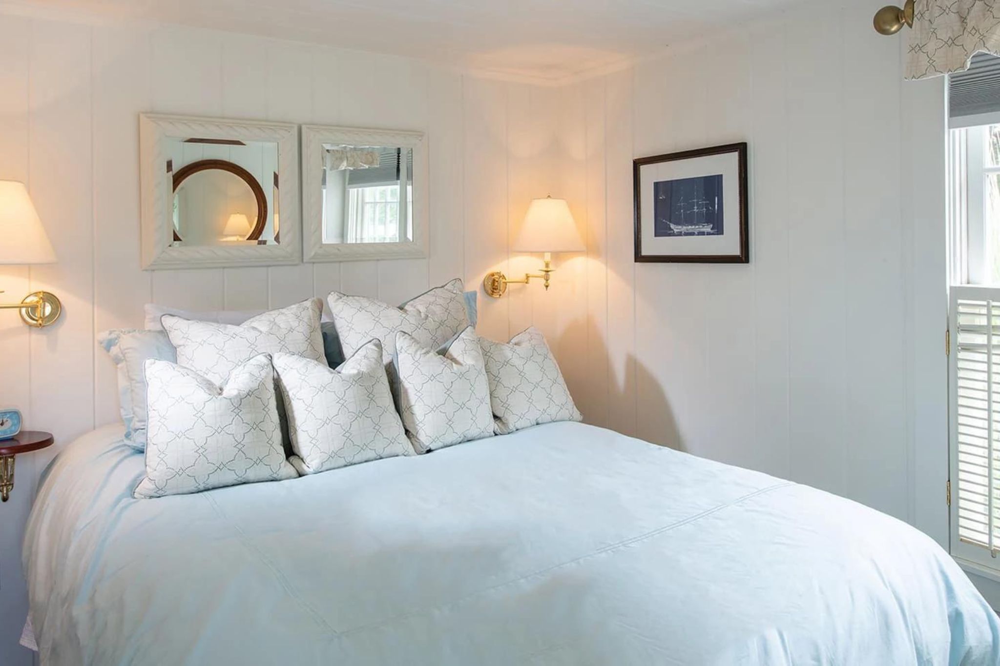 Cozy bedroom with white bedding, decorative pillows, and wall art.