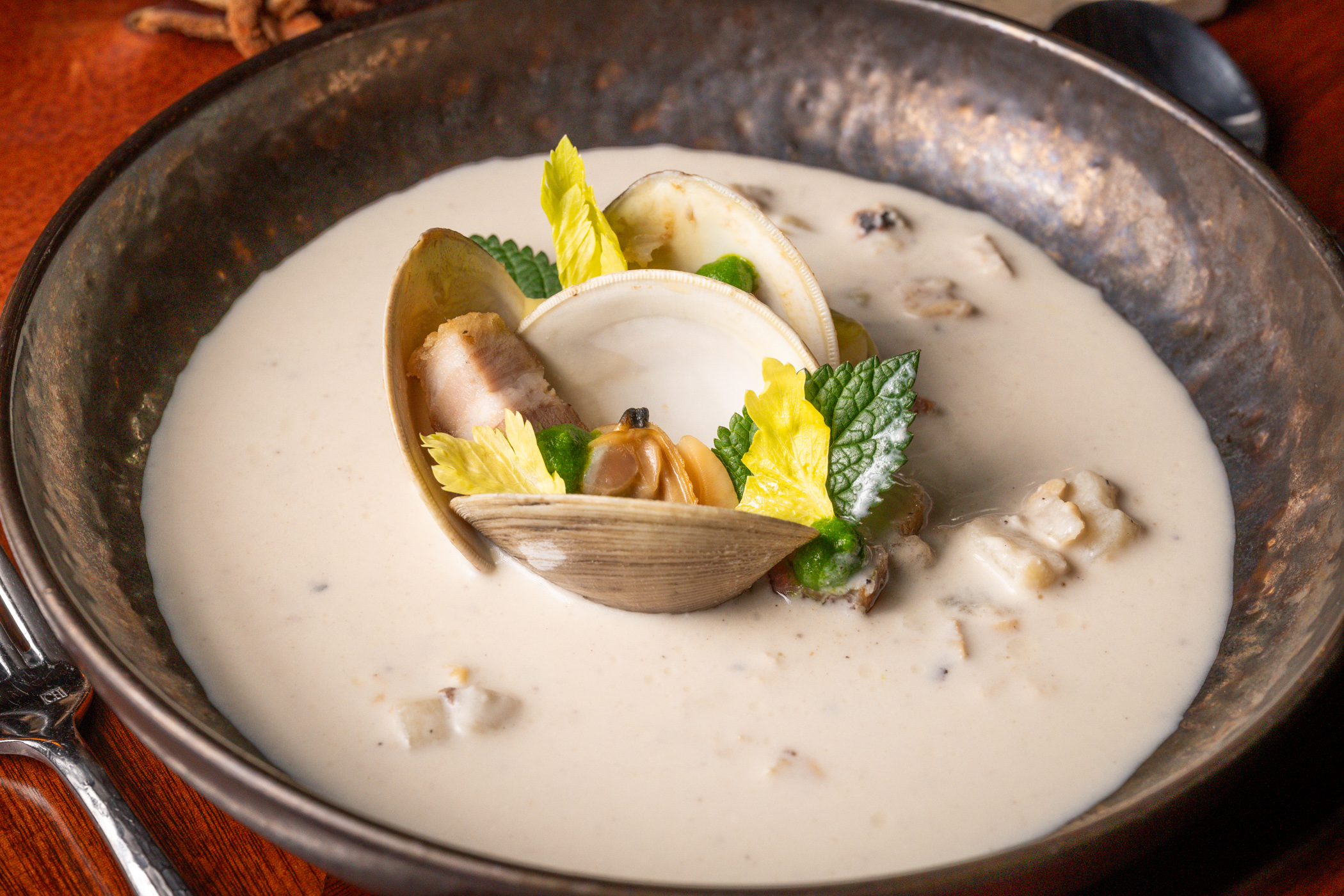 Creamy clam chowder garnished with herbs and celery in a rustic bowl.