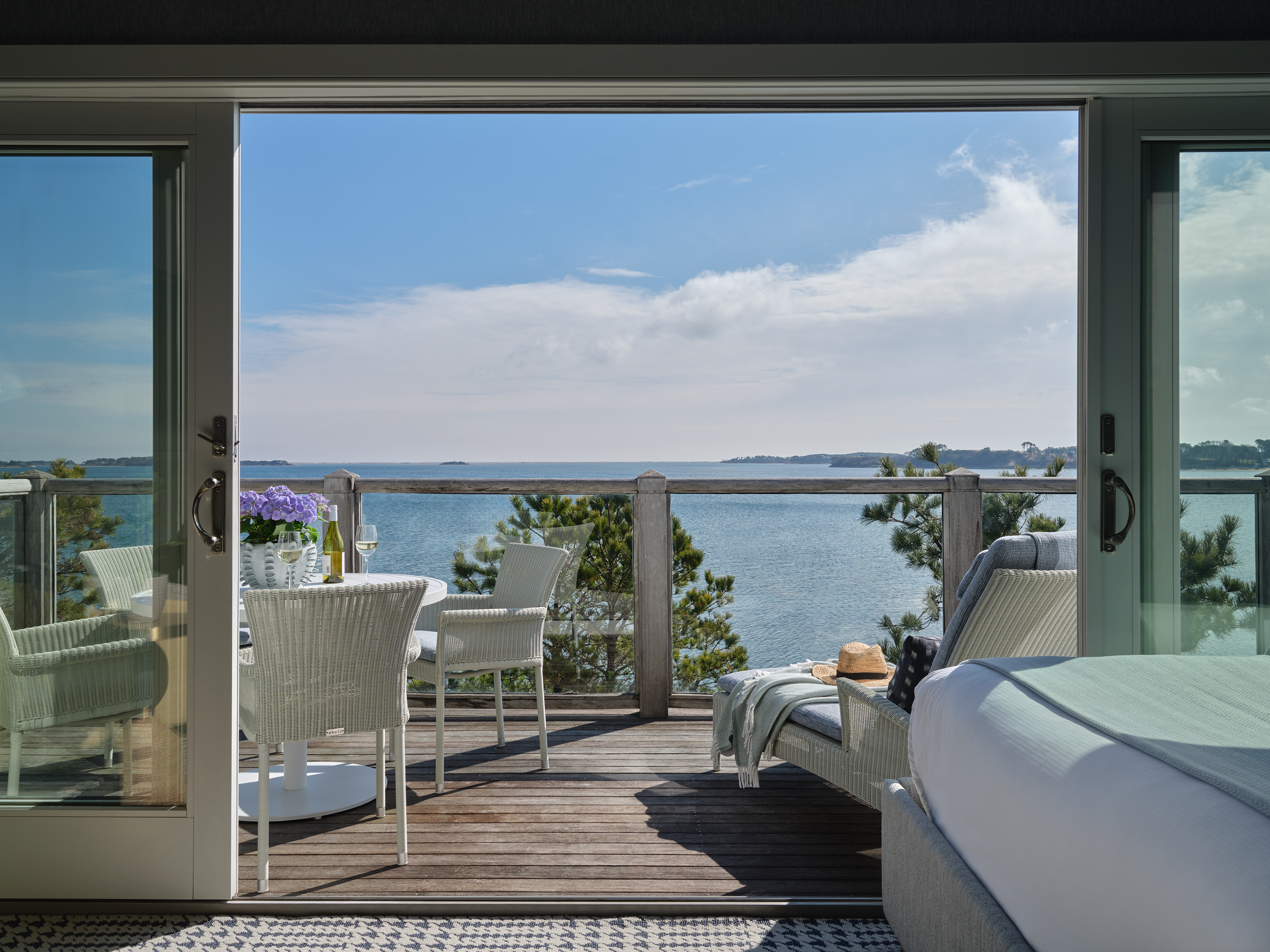 Open balcony doors with ocean view, white furniture, sunny sky.