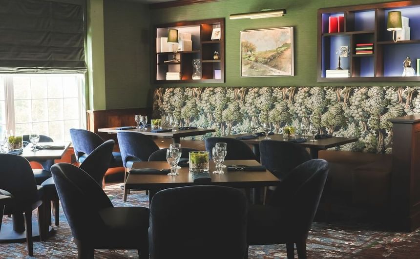 Cozy restaurant interior with dark chairs, floral wall, and shelves with books.