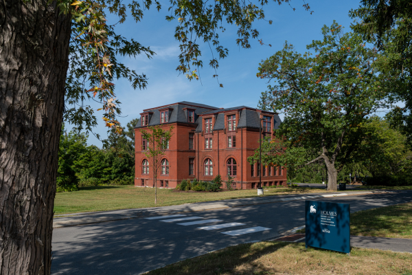 Red brick building with a mansard roof, trees, and a street in the foreground.