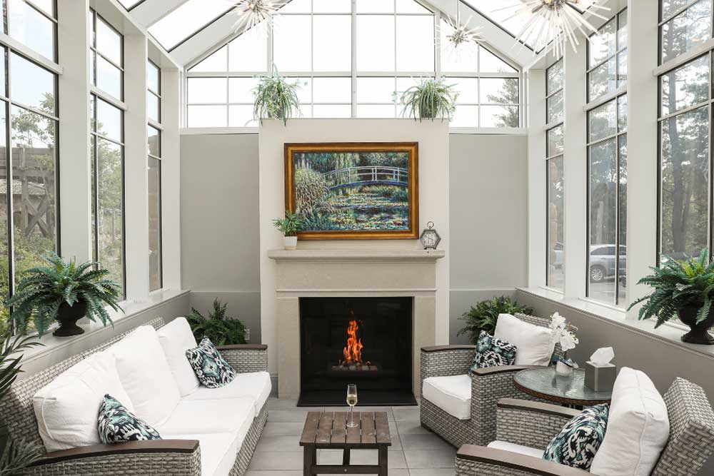Sunlit living room with white sofas, fireplace, and potted plants.