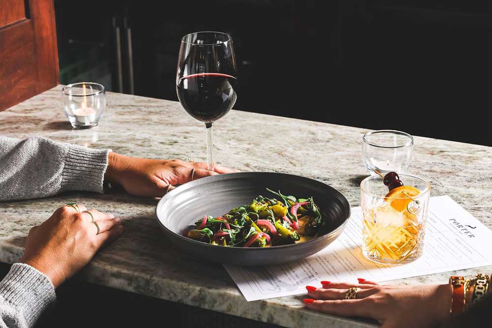 Hands on a marble table with salad, red wine, and cocktail.