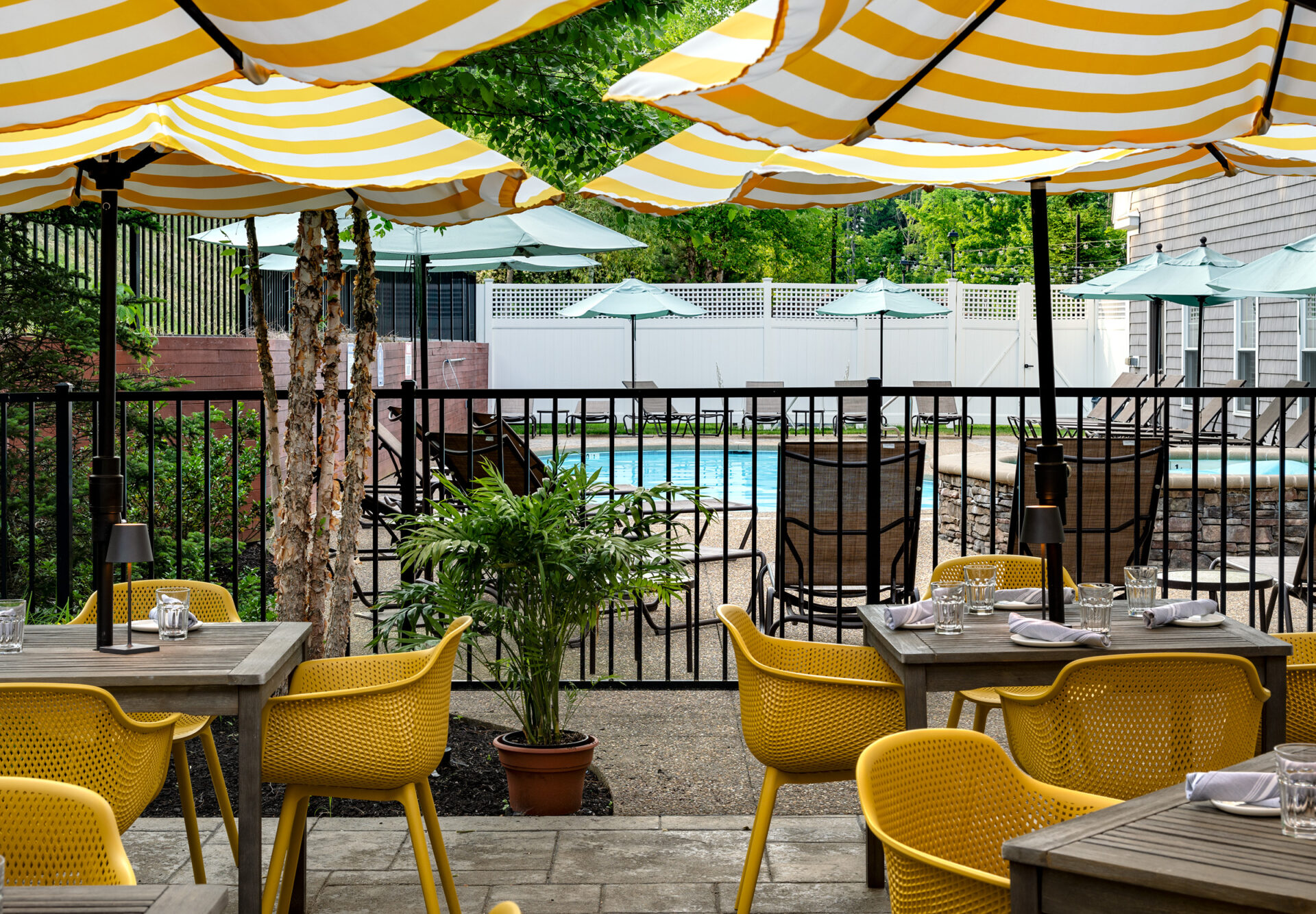 Outdoor patio dining with yellow chairs, striped umbrellas, and pool view.