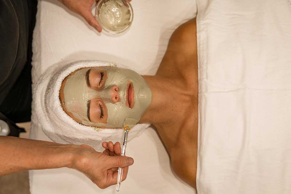 Facial spa treatment with clay mask applied by a therapist.