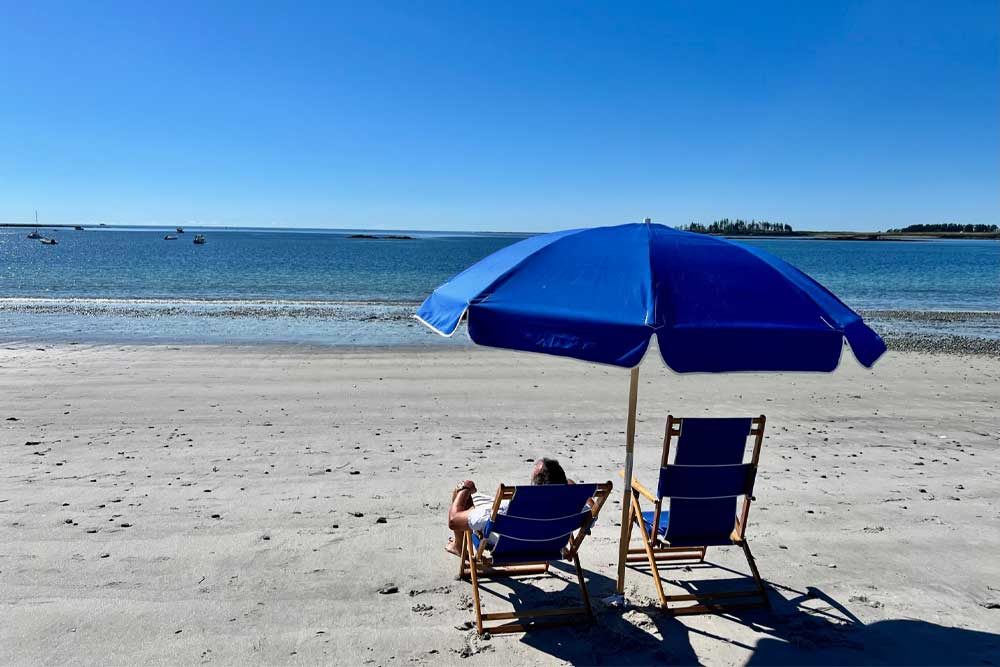 Two beach chairs and a blue umbrella on a sunny, tranquil beach.