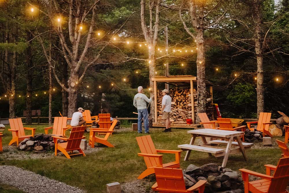 Outdoor seating area with orange chairs, string lights, and people chatting at dusk.