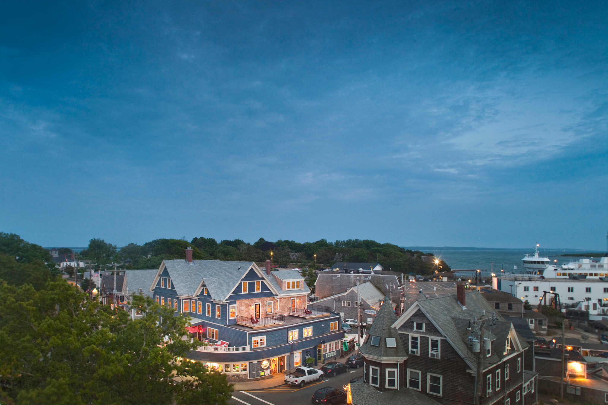 Aerial view of a coastal town at dusk with lit-up buildings and the ocean in the background.