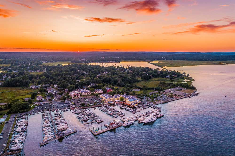 Aerial view of a marina at sunset, with boats docked and an orange-pink sky.