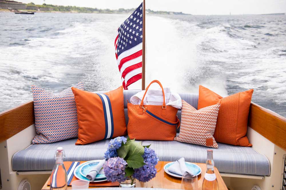 Cozy boat seating area with orange pillows and U.S. flag, table with hydrangeas and bottles.