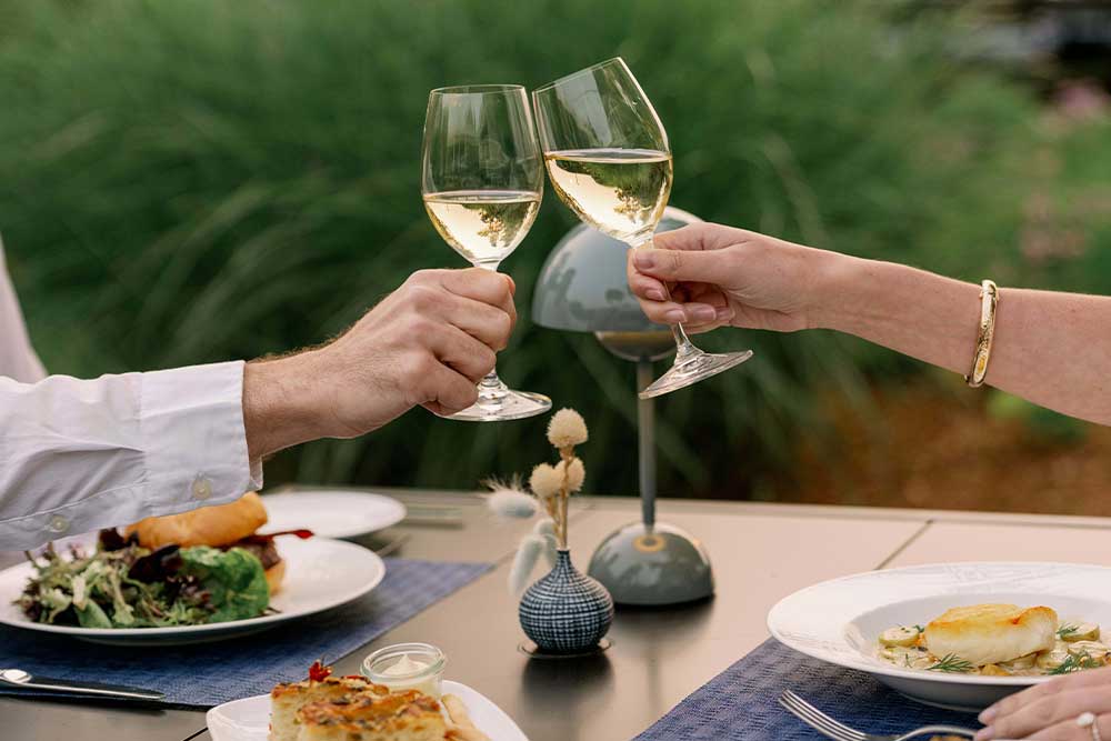 Clinking wine glasses over a dining table with food.
