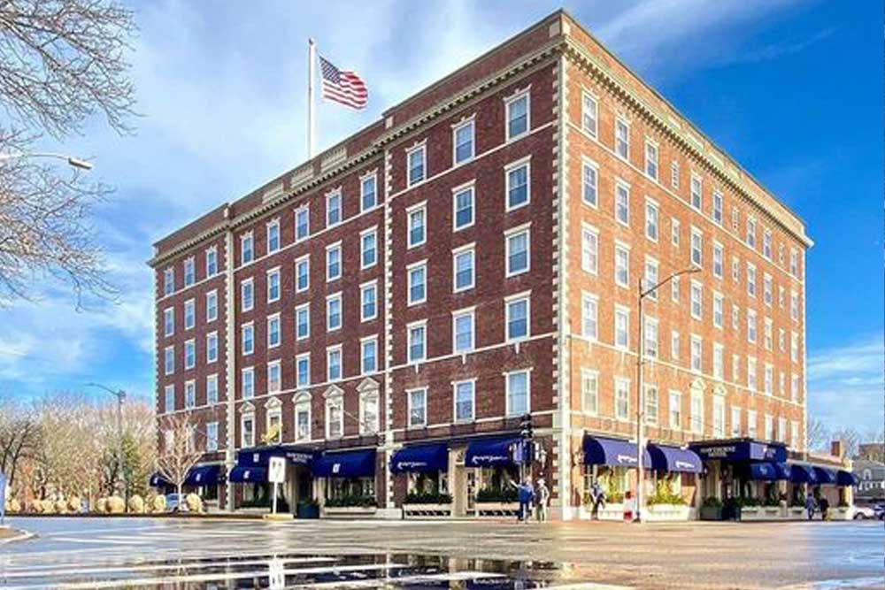 Brick hotel with blue awnings, American flag on top, clear blue sky.