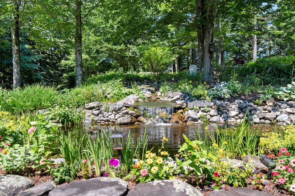 Garden with vibrant flowers and small waterfall, surrounded by lush greenery.