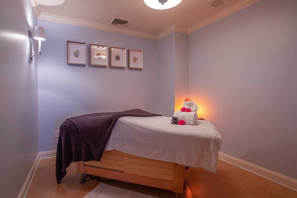 Massage room with a table, dim lighting, and soft purple walls.