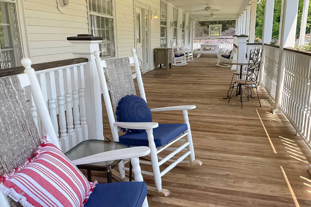 Long porch with white rocking chairs and wood flooring, under a covered veranda.