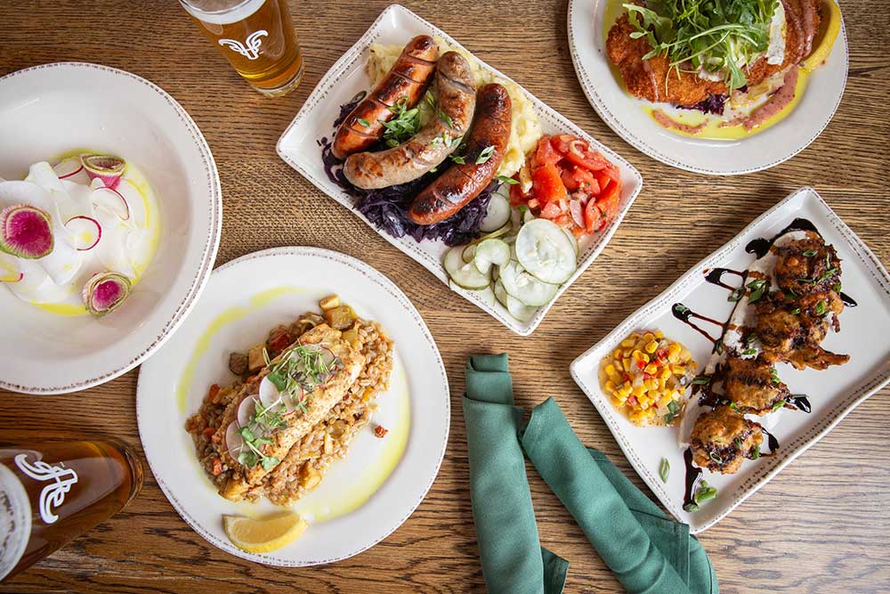 A table with various plated dishes, including sausage, pasta, and a salad.