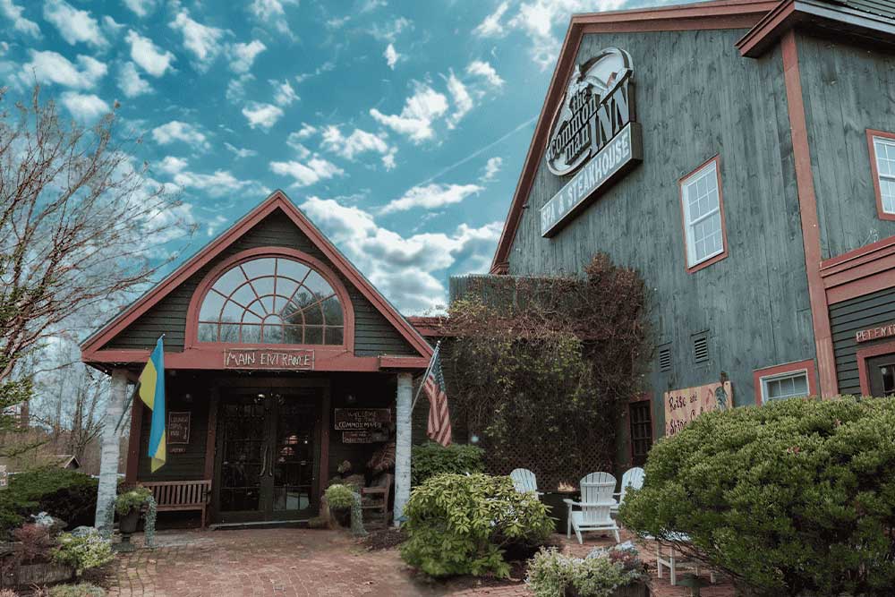 Rustic building with flags and greenery under a cloudy sky.