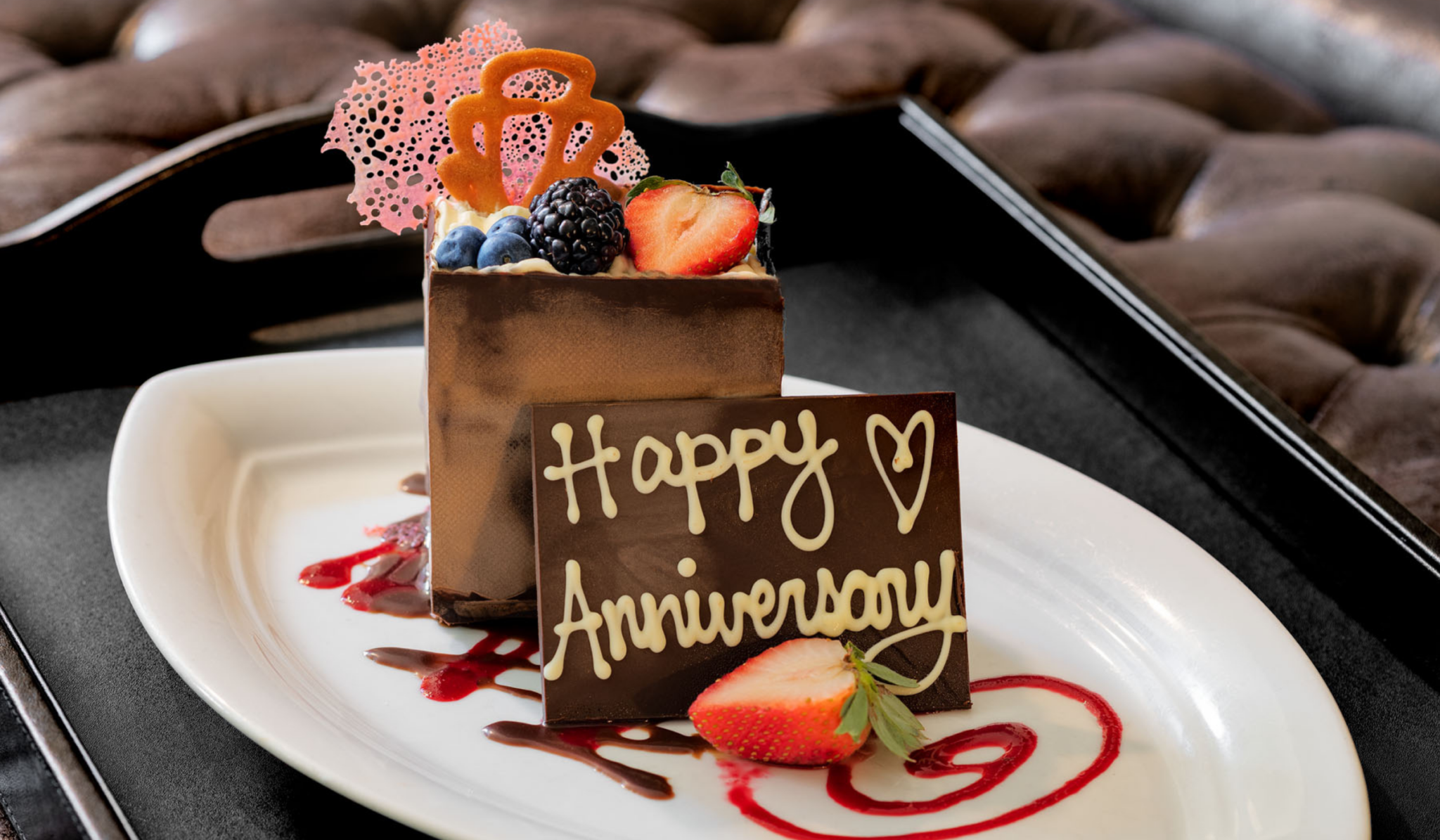 Chocolate dessert with berries and "Happy Anniversary" note on a white plate.