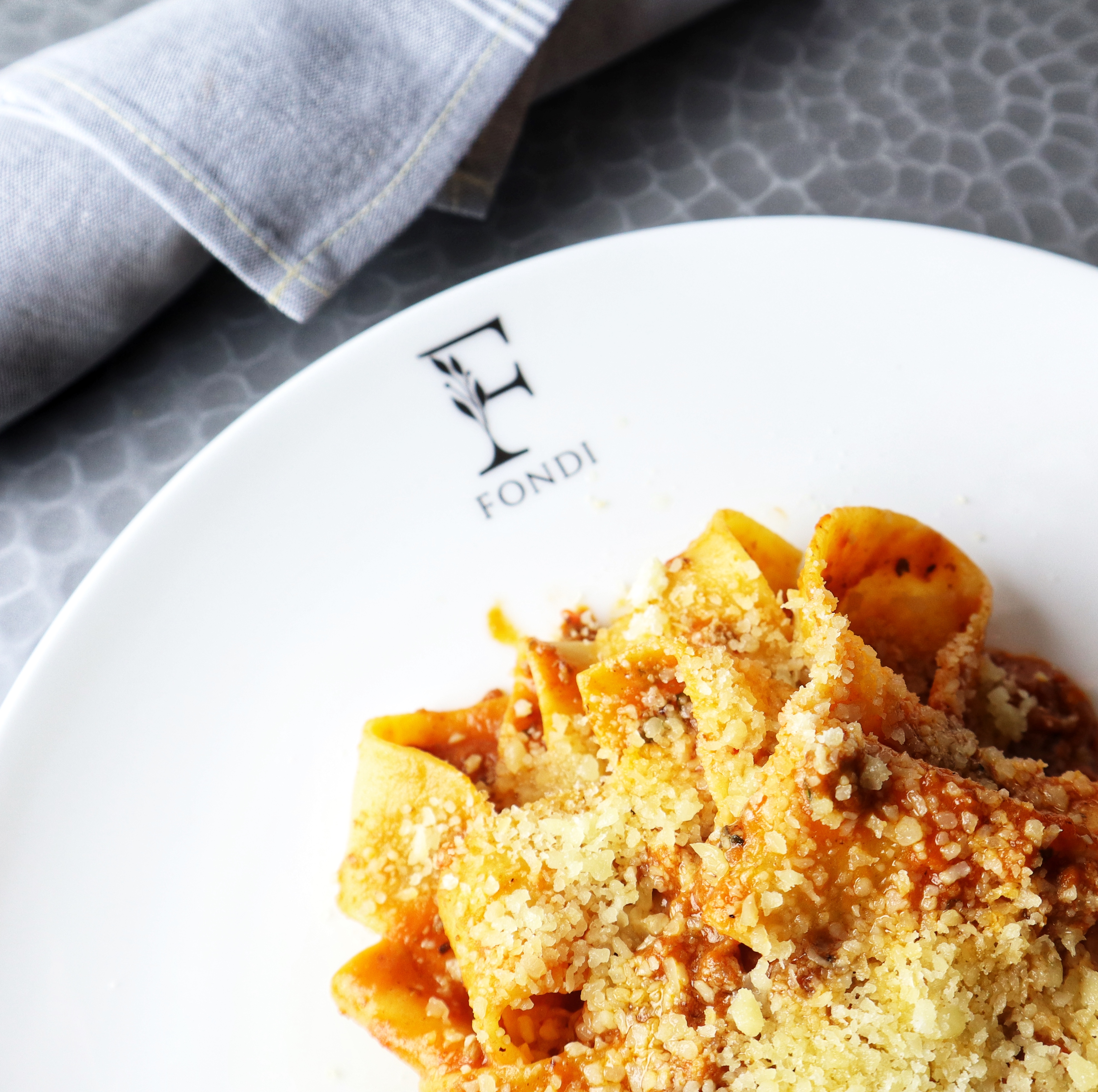 Pasta with tomato sauce and cheese on a white plate next to a folded napkin.