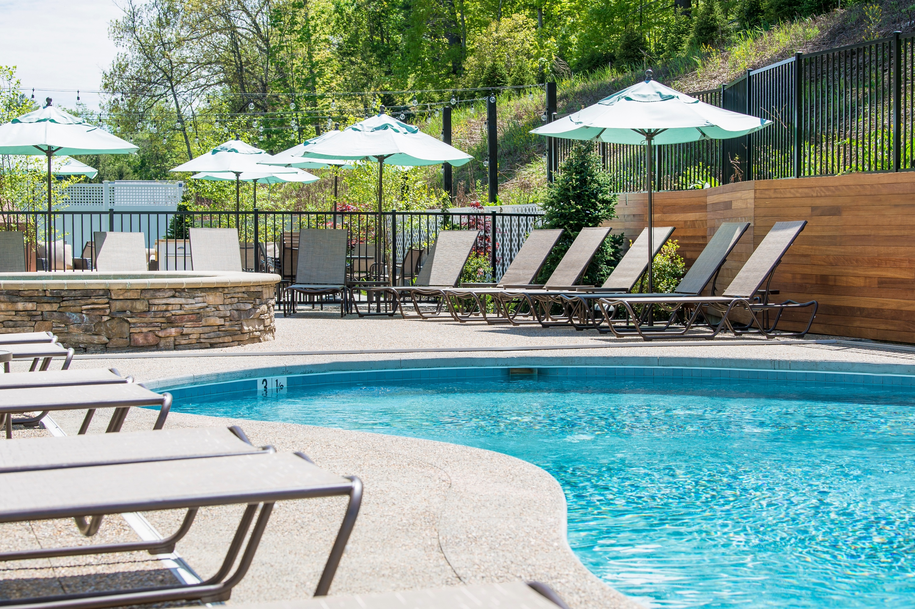 Sunlit poolside with lounge chairs and umbrellas.