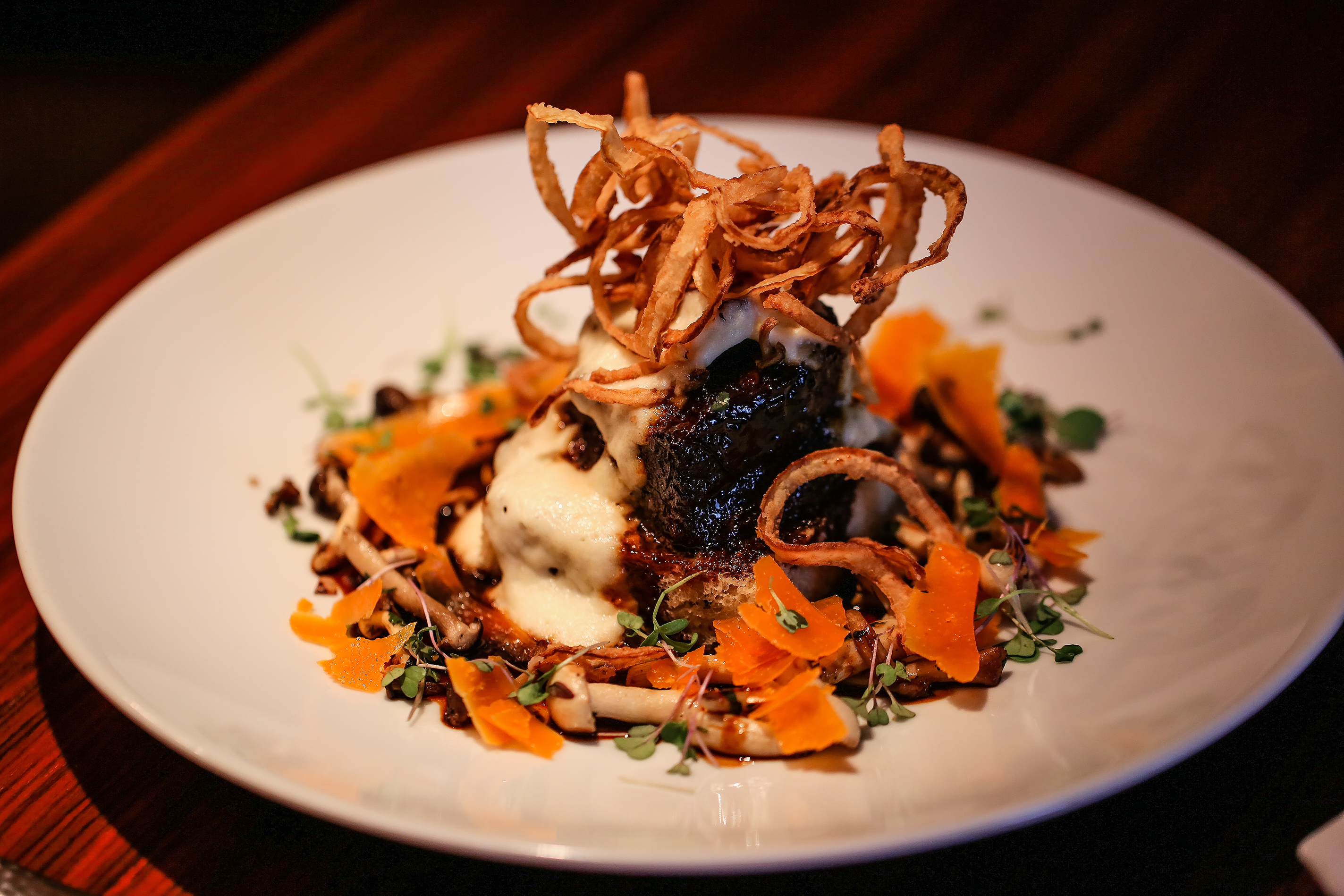 Gourmet dish with crispy onions, purée, and colorful garnish on a white plate.