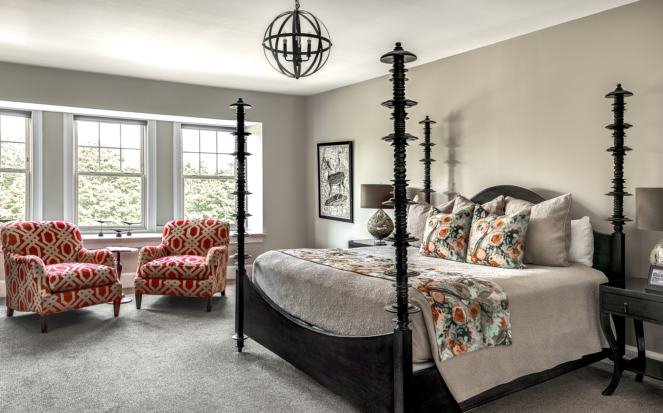 Elegant bedroom with patterned armchairs, four-poster bed, and large windows.