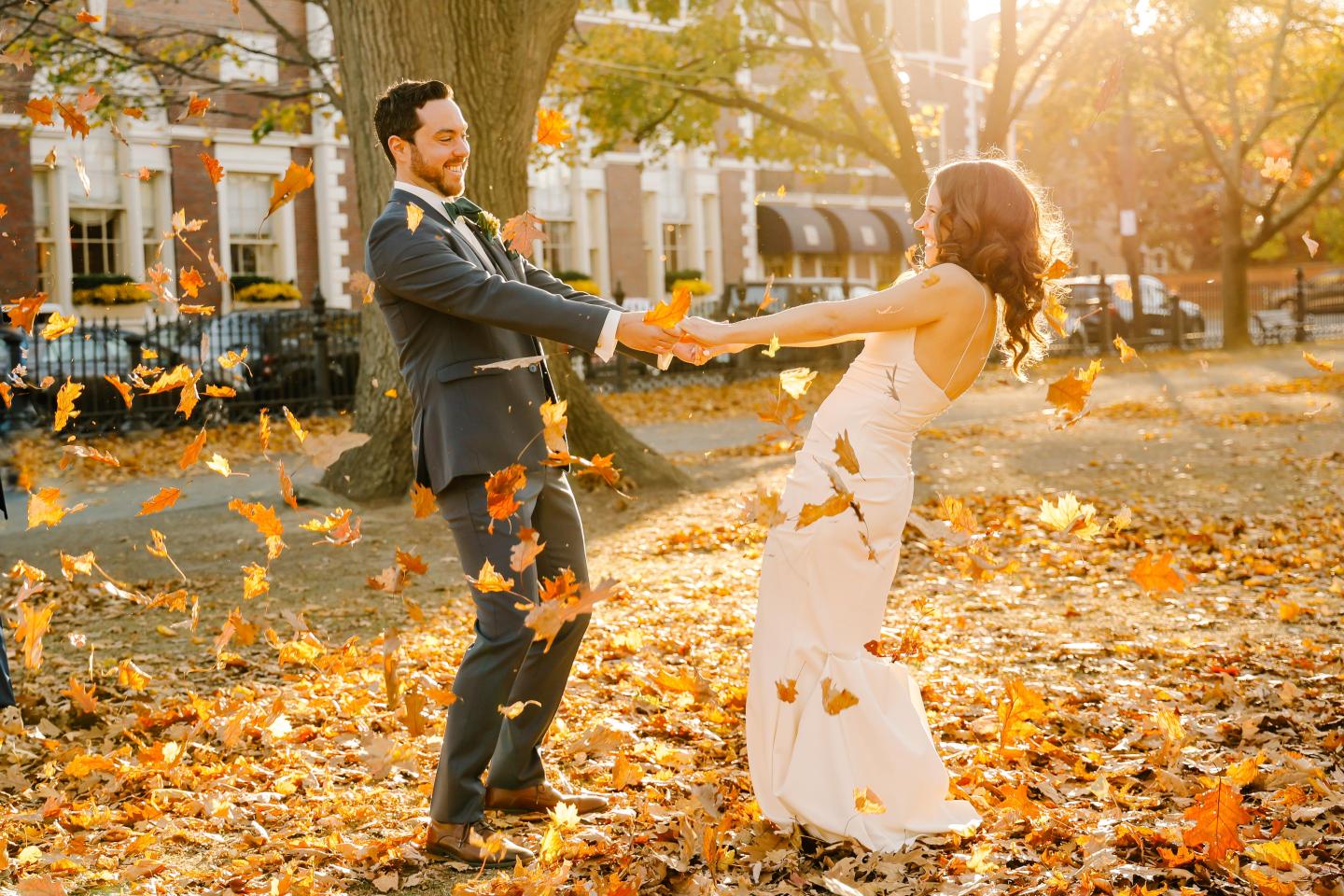 Couple joyfully dancing in autumn leaves under warm sunlight.