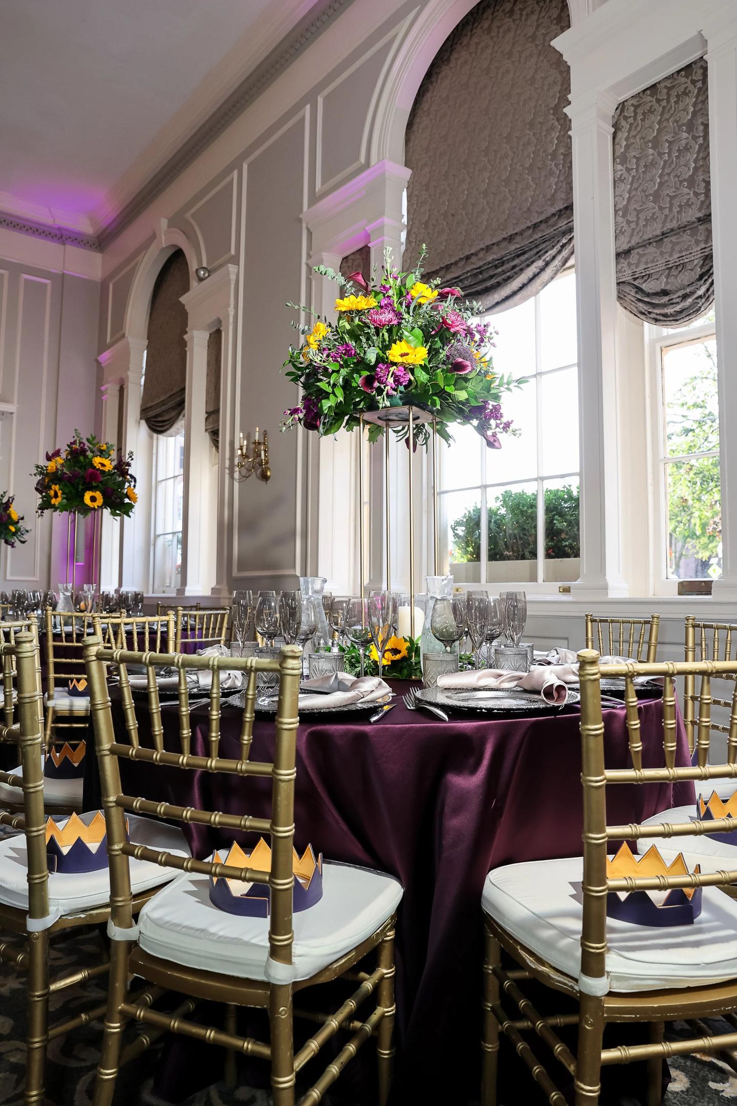 Elegant dining room with purple tablecloth and floral centerpieces.