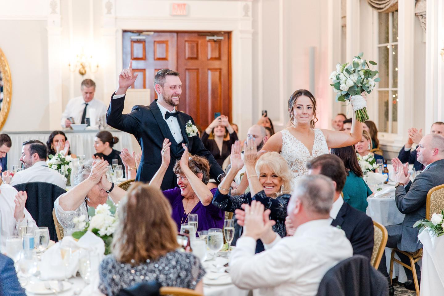 Wedding reception with bride and groom entering, guests applauding.