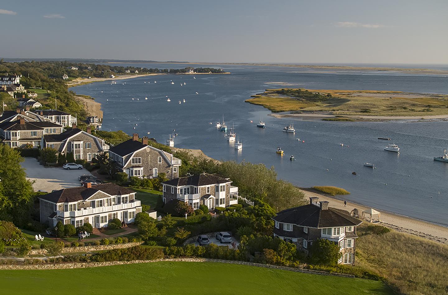 Coastal village with houses, river, and boats under a clear sky.