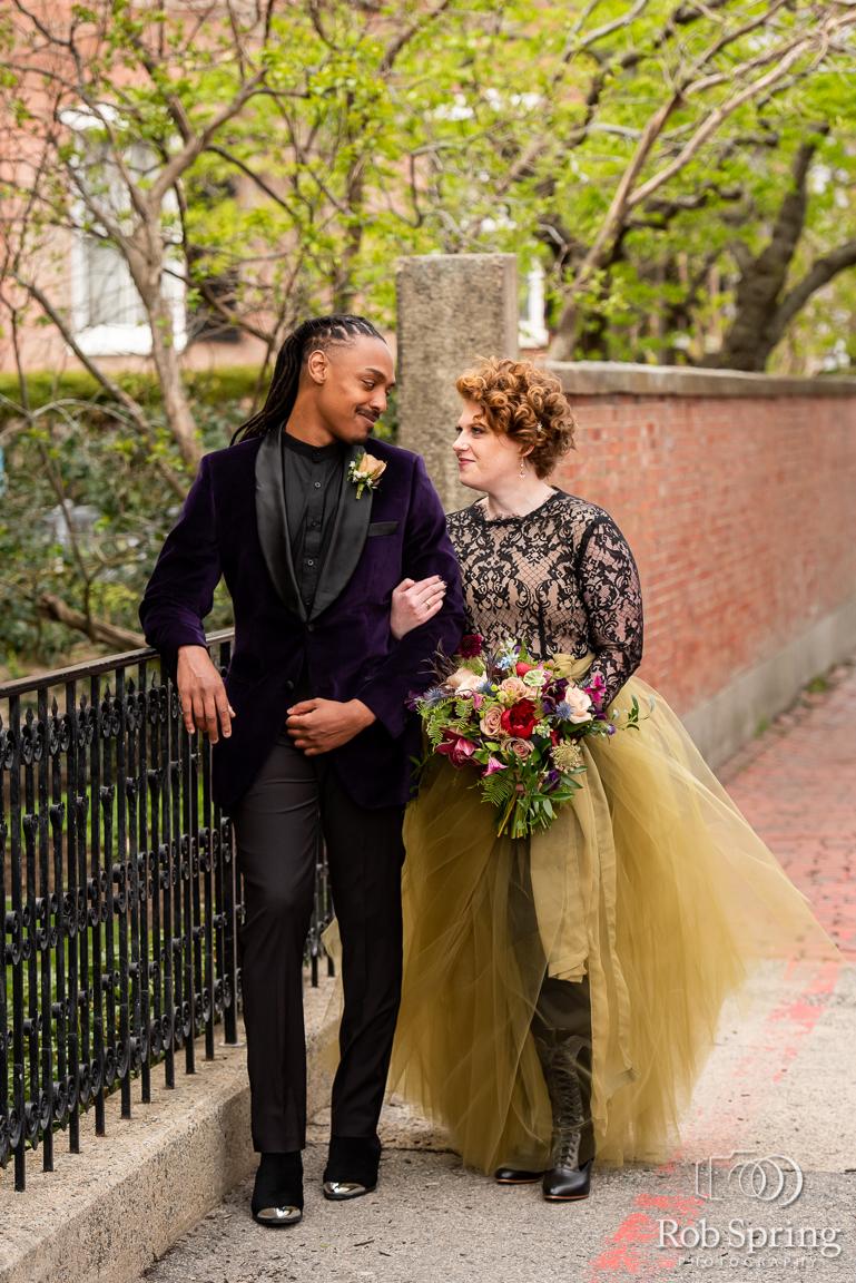 Two people in formal attire walking, smiling at each other, with a bouquet.
