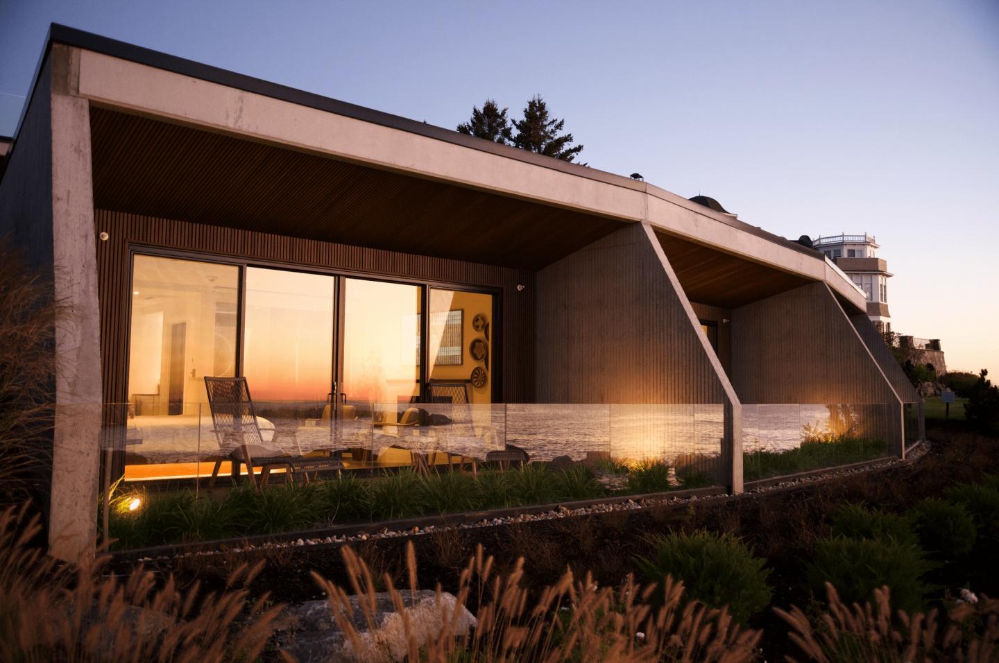 Modern room exterior at sunset with large glass windows and landscaped yard.