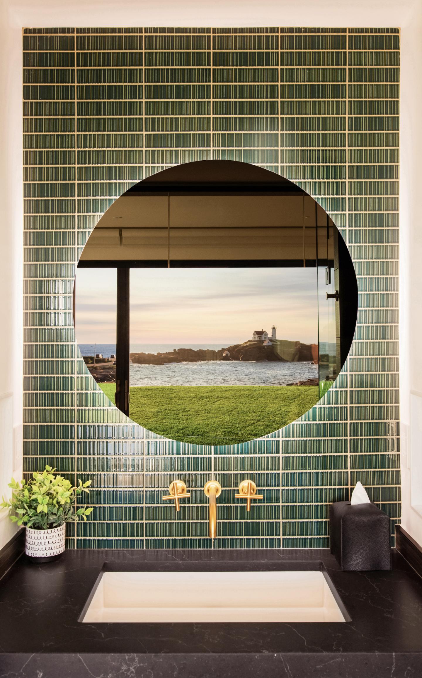 Green tiled wall with circular mirror reflecting a lake view.
