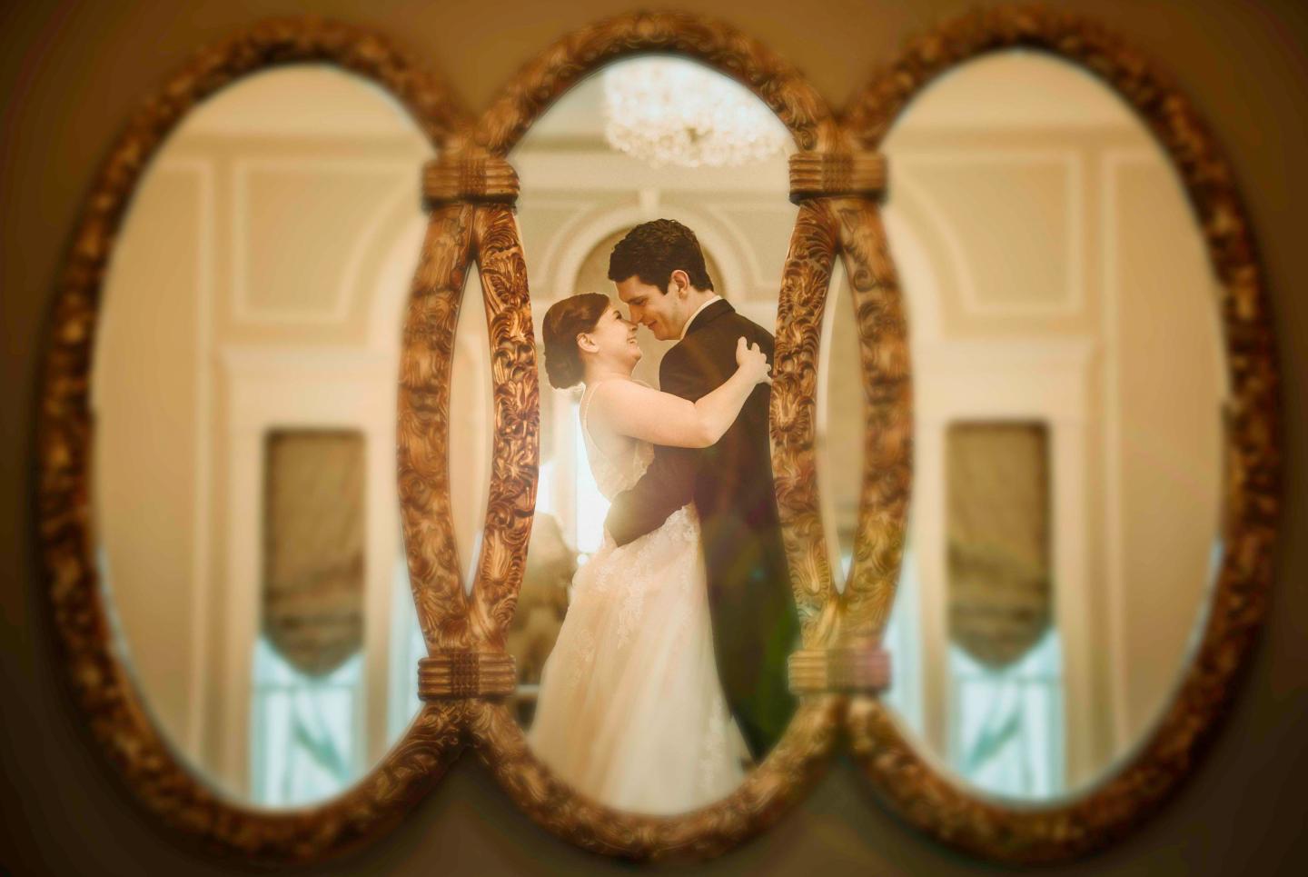 Couple embraces in ornate oval mirrors, soft lighting.