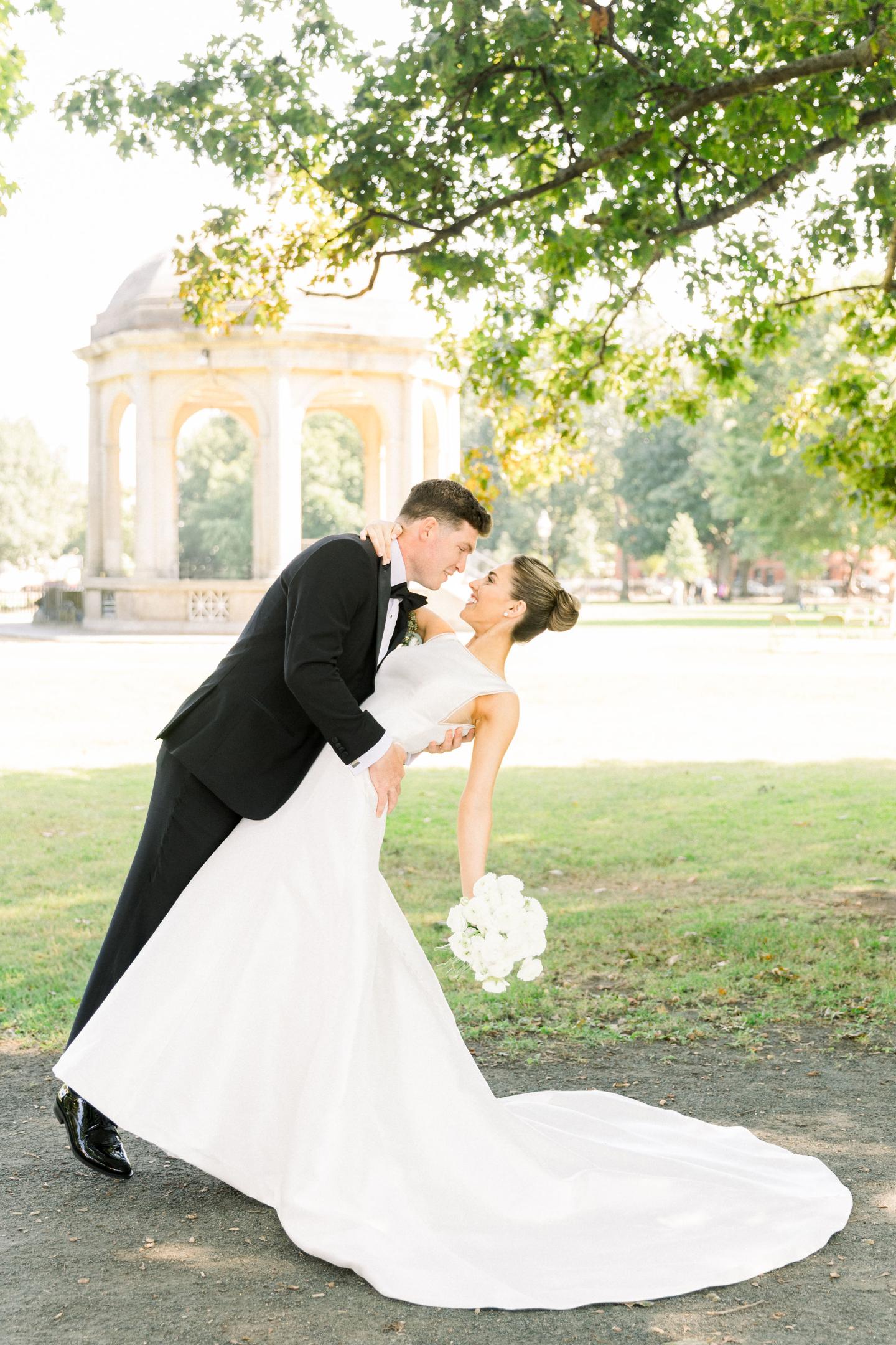Bride and groom dancing outdoors under a tree, with a gazebo in the background.