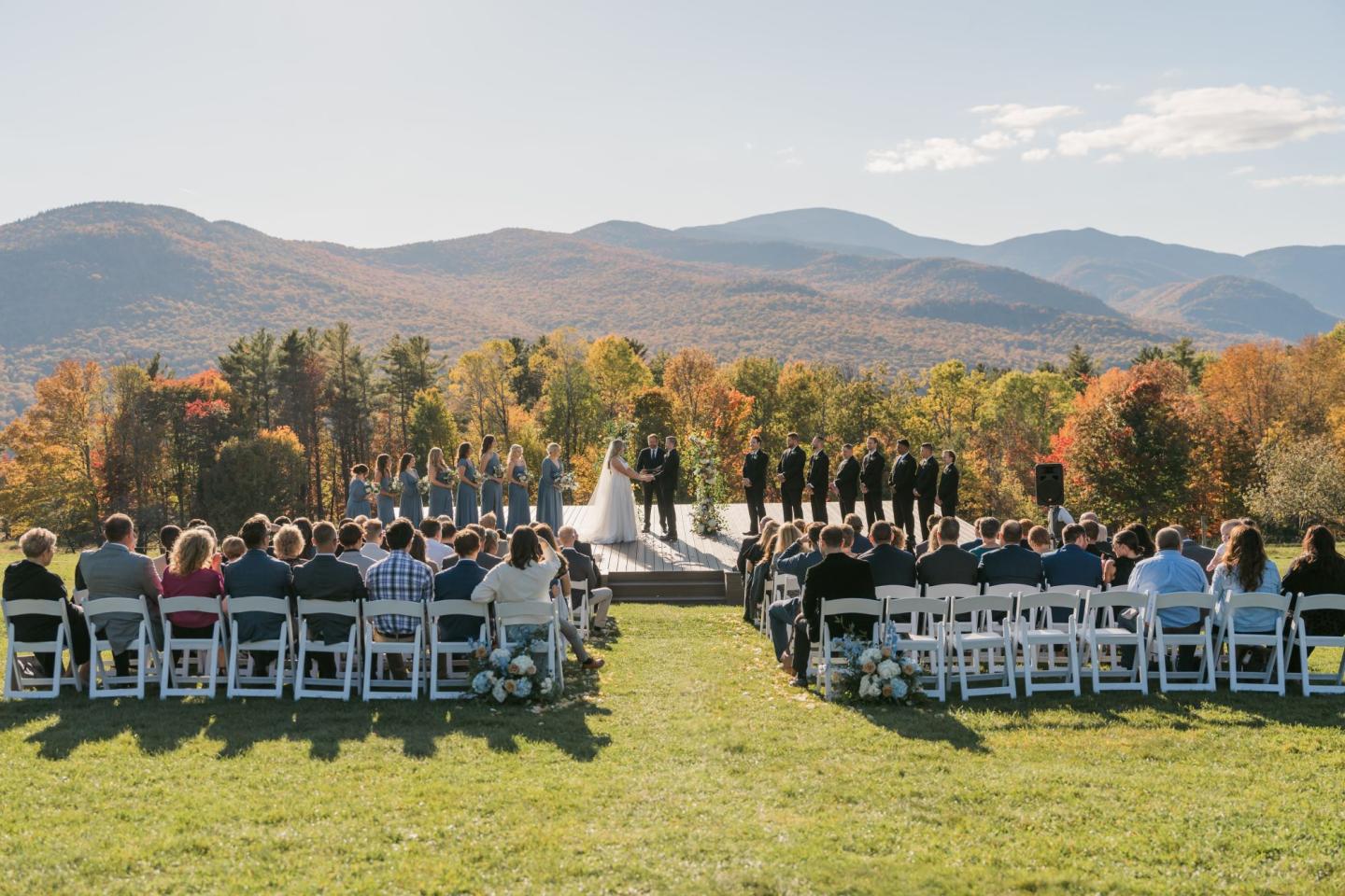 Outdoor wedding with mountains in the background, guests seated in rows.