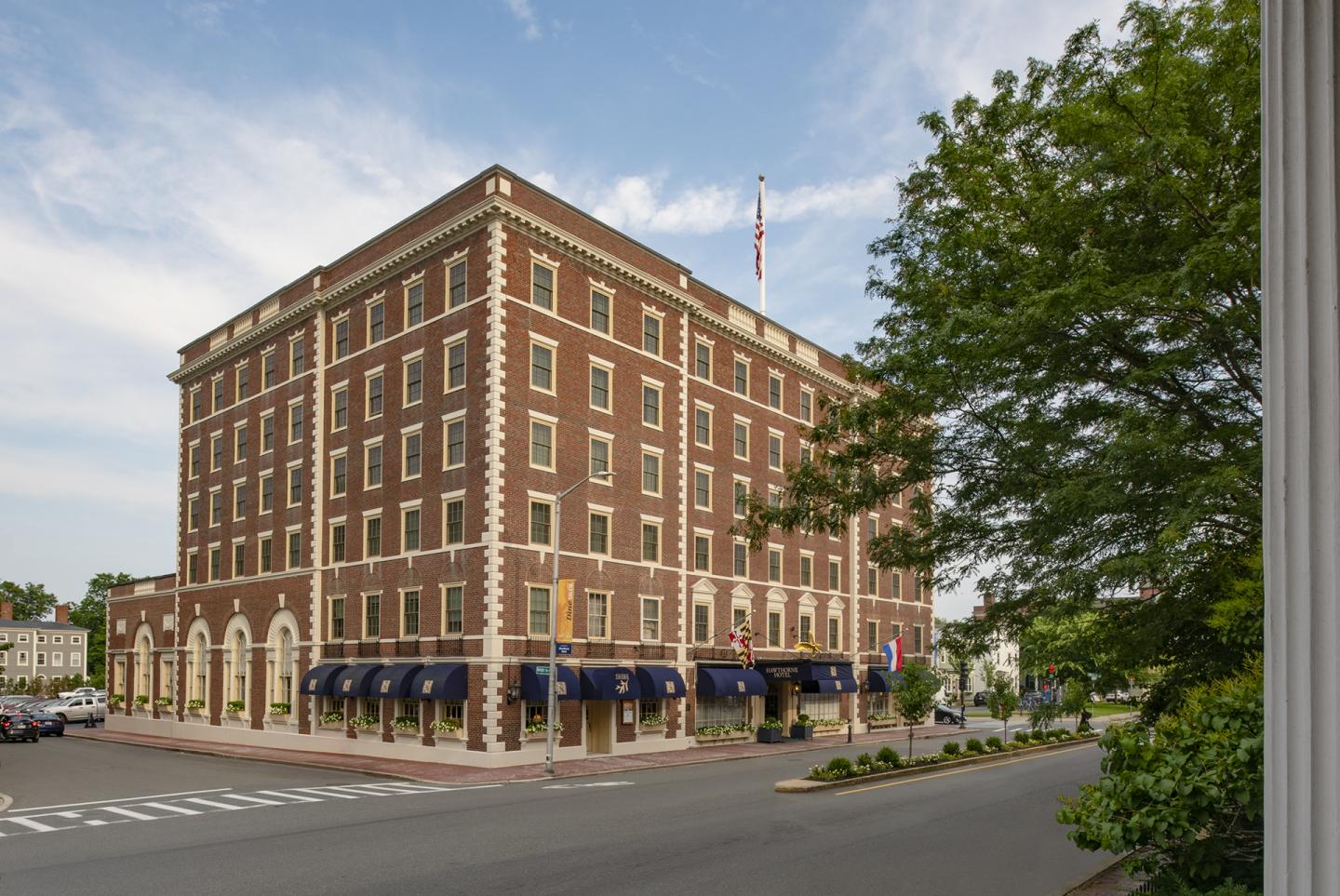 Brick hotel with blue awnings on a sunny day, surrounded by trees.