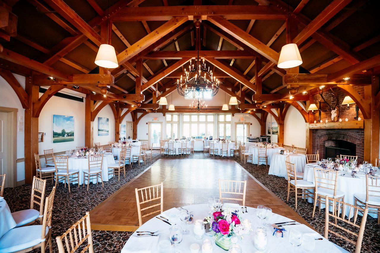 Bright banquet hall with wooden beams, set for an event with round tables and chairs.
