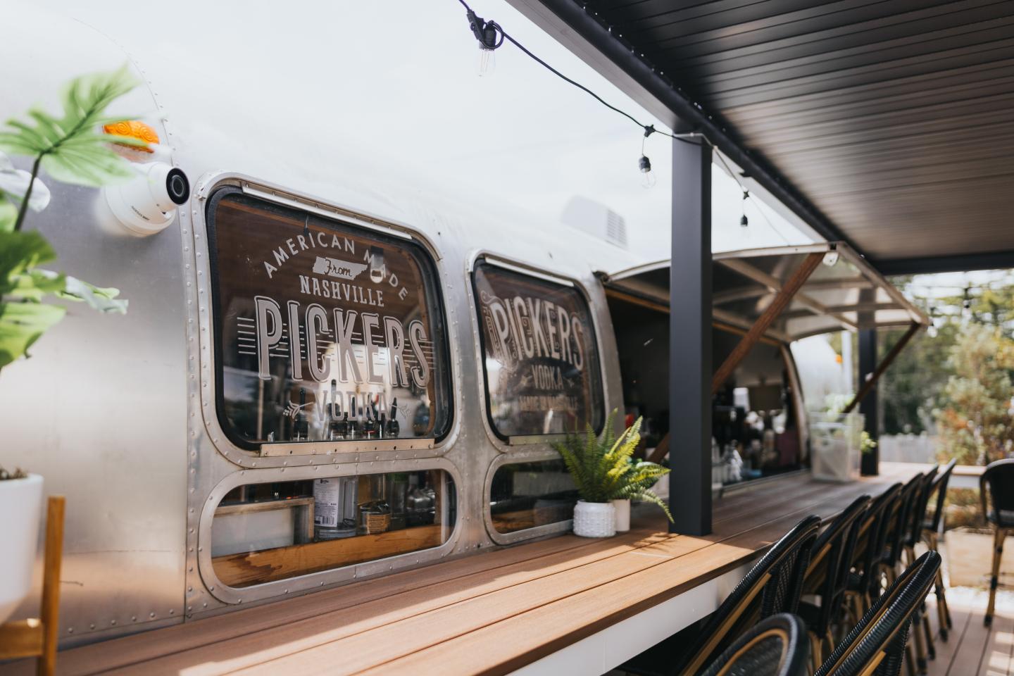 Silver food truck with outdoor seating and plants.