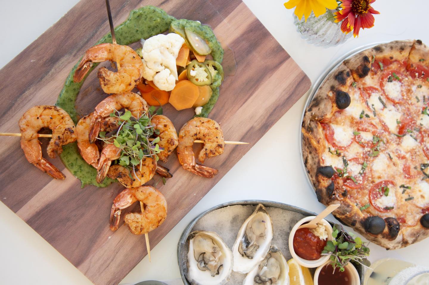 Grilled shrimp, oysters, and pizza on a table with colorful garnish.