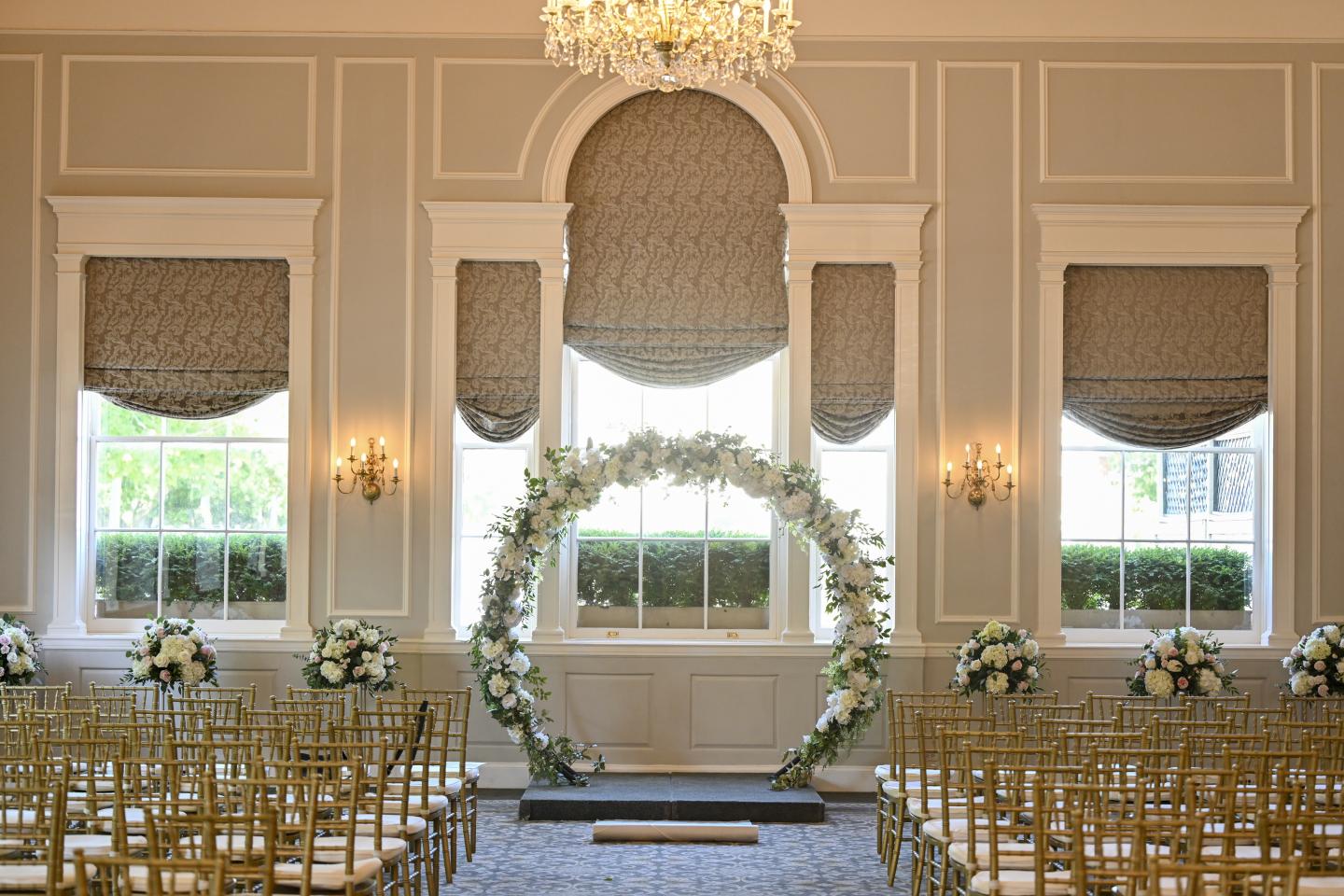 Elegant wedding venue with gold chairs, floral arch, and chandelier.