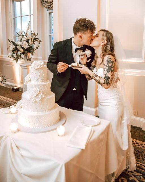 Couple kissing beside a tiered wedding cake in an elegant room.