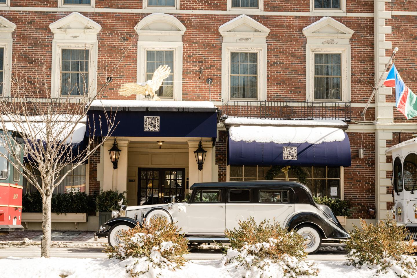 Vintage car parked outside a brick building with blue awnings in a snowy setting.